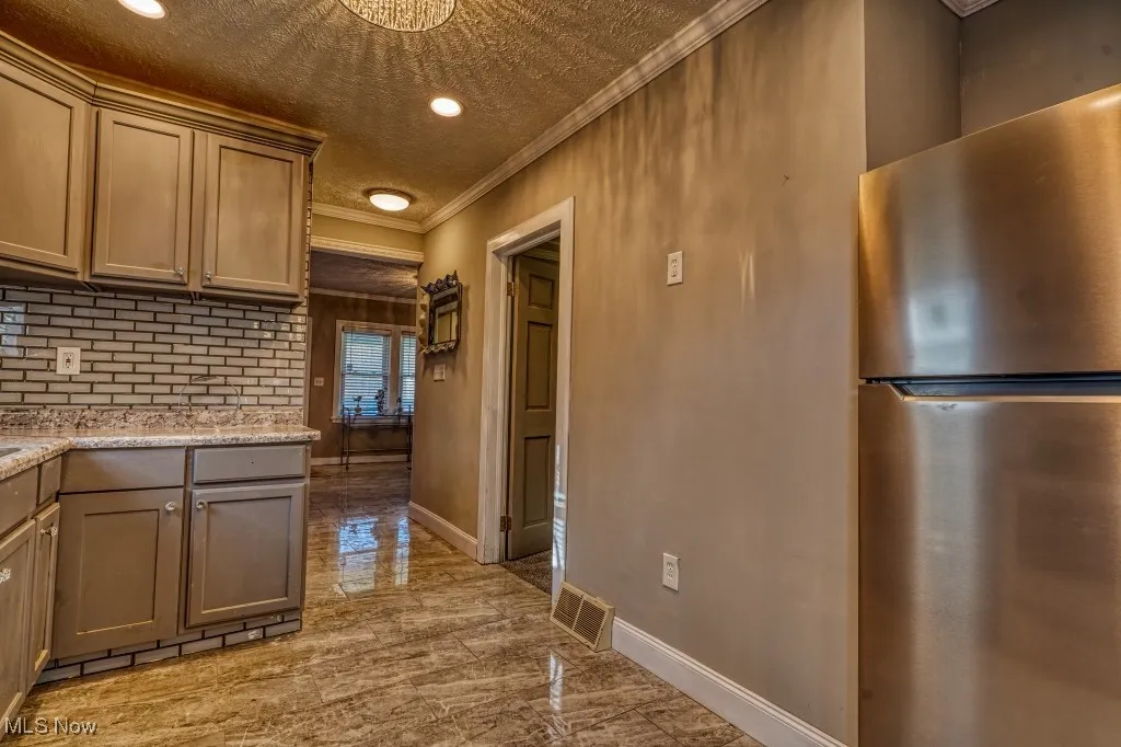 Kitchen featuring freestanding refrigerator, crown molding, light marble finish floors, recessed lighting, and a textured ceiling