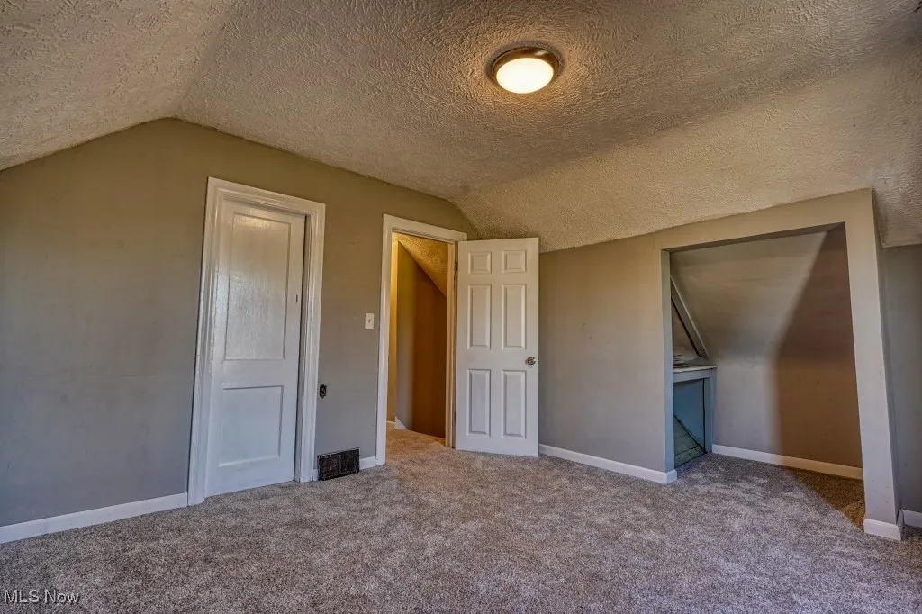 Unfurnished bedroom with lofted ceiling, carpet, and a textured ceiling