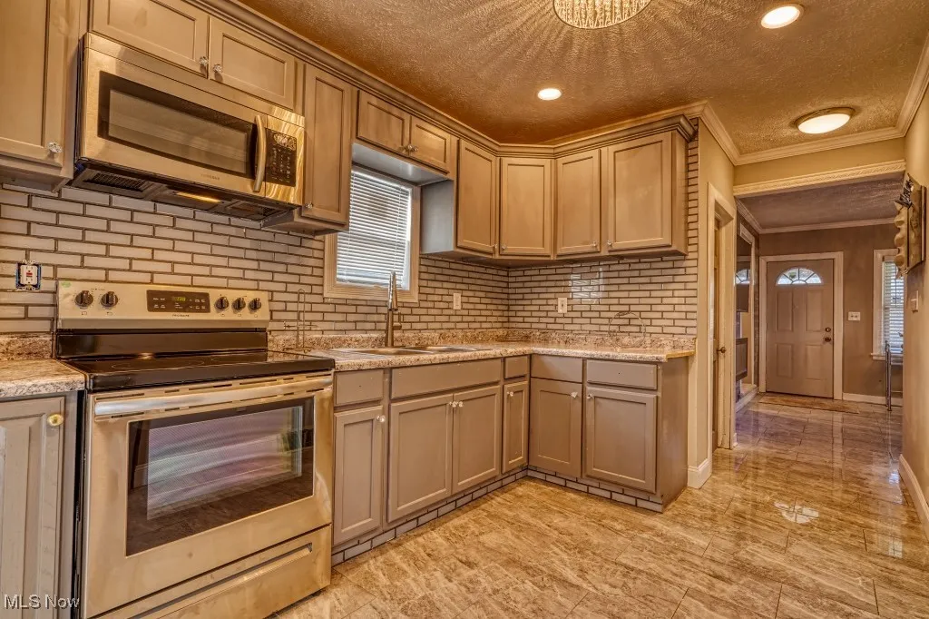 Kitchen featuring appliances with stainless steel finishes, crown molding, light countertops, a textured ceiling, and tasteful backsplash
