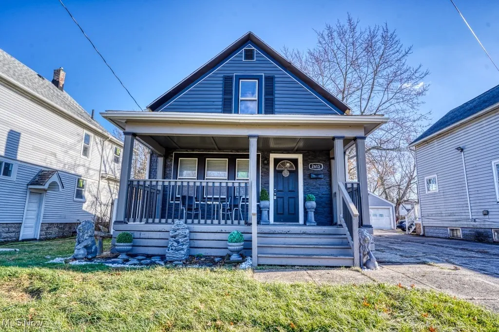View of front of property featuring a porch, a garage, an outdoor structure, and a front lawn