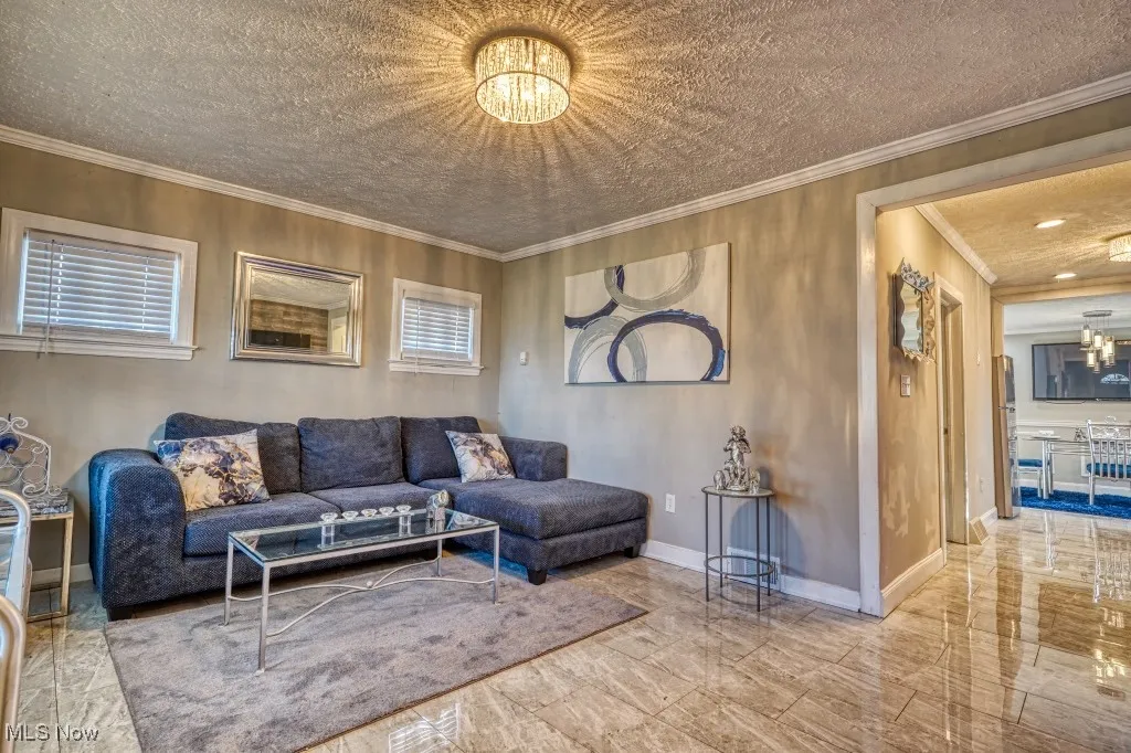 Living area featuring a chandelier, marble look tiles, a textured ceiling, and crown molding