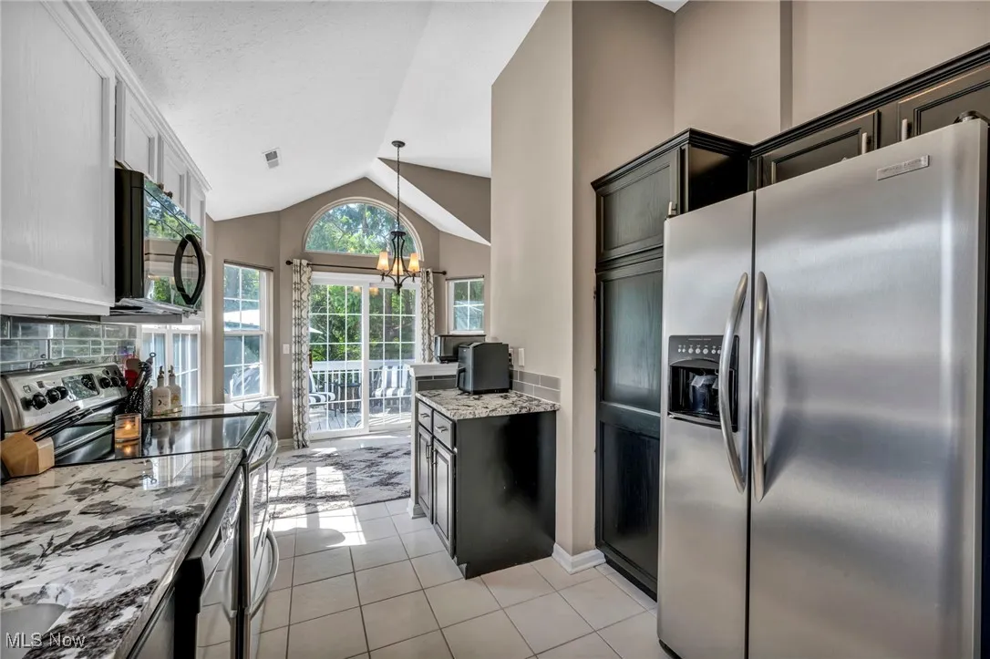 Kitchen with stainless steel appliances, a chandelier, vaulted ceiling, light stone countertops, and light tile patterned flooring