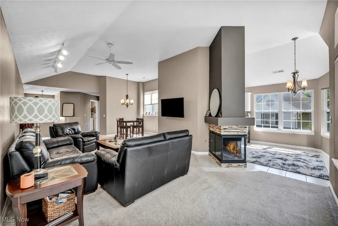 Living room with a chandelier, lofted ceiling, track lighting, a ceiling fan, and a multi sided fireplace