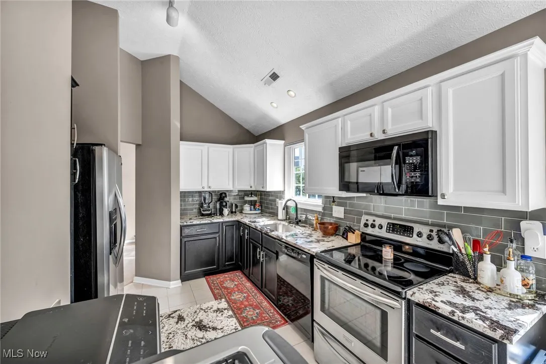 Kitchen with black appliances, white cabinets, light tile patterned floors, lofted ceiling, and decorative backsplash