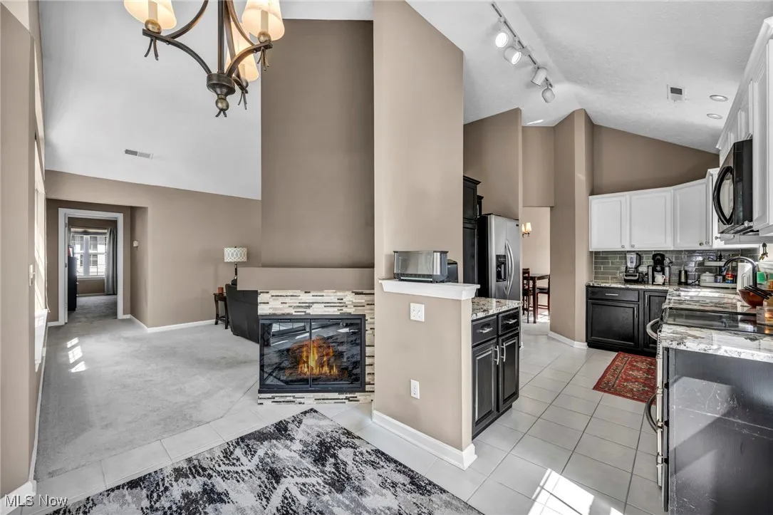Kitchen featuring light tile patterned floors, high vaulted ceiling, track lighting, white cabinets, and light stone counters
