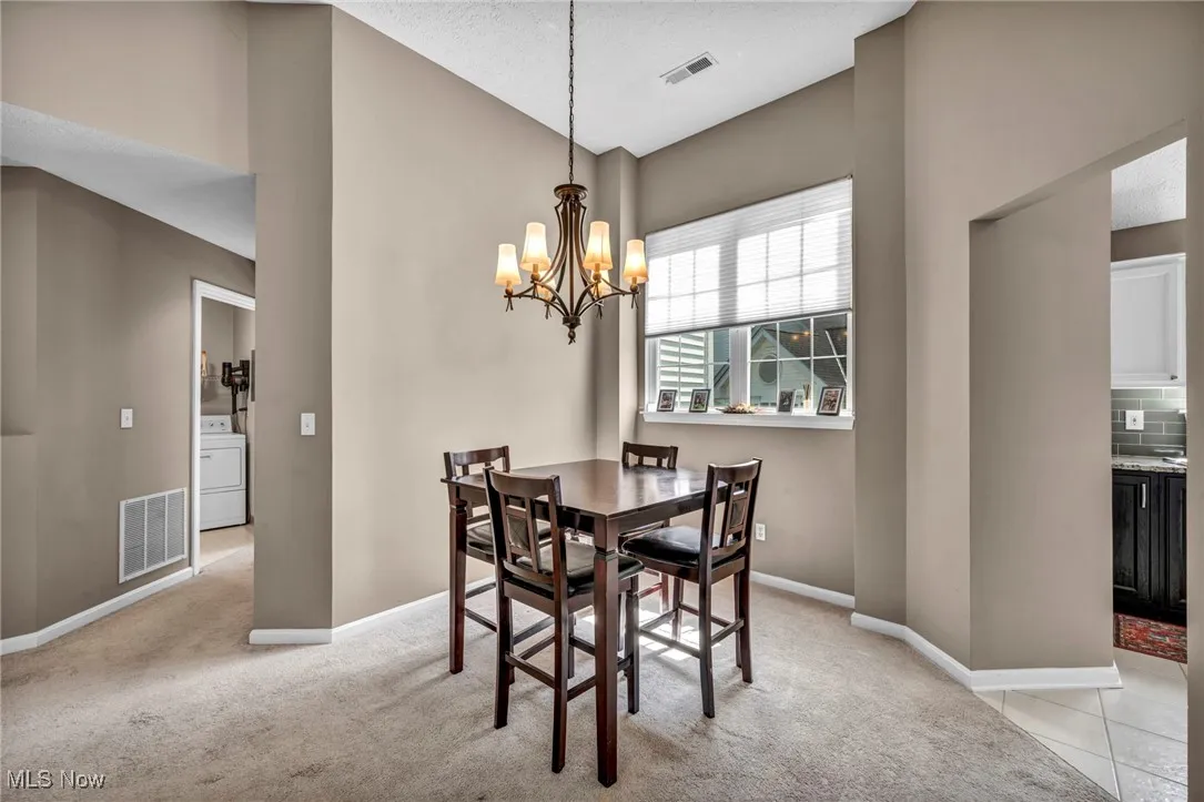Dining space featuring washer / dryer, a chandelier, light colored carpet, and high vaulted ceiling