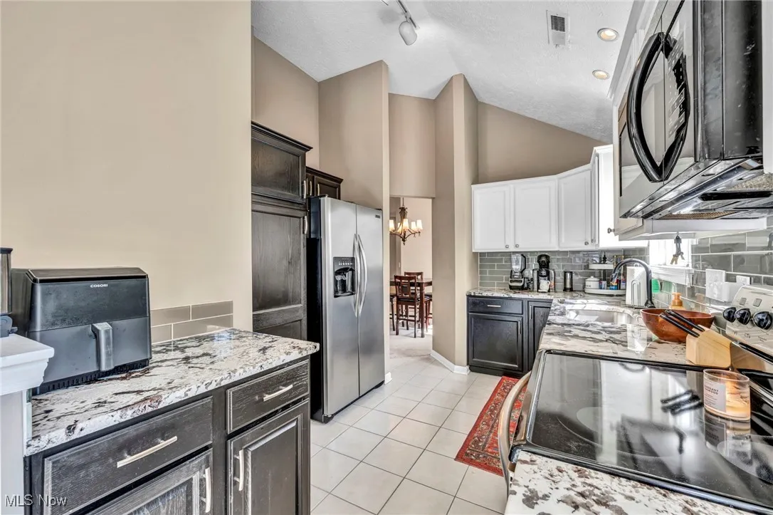 Kitchen featuring black appliances, light stone counters, tasteful backsplash, a chandelier, and light tile patterned floors