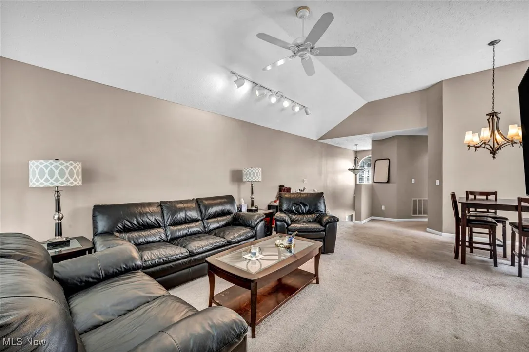 Living room featuring a chandelier, lofted ceiling, ceiling fan, light colored carpet, and rail lighting