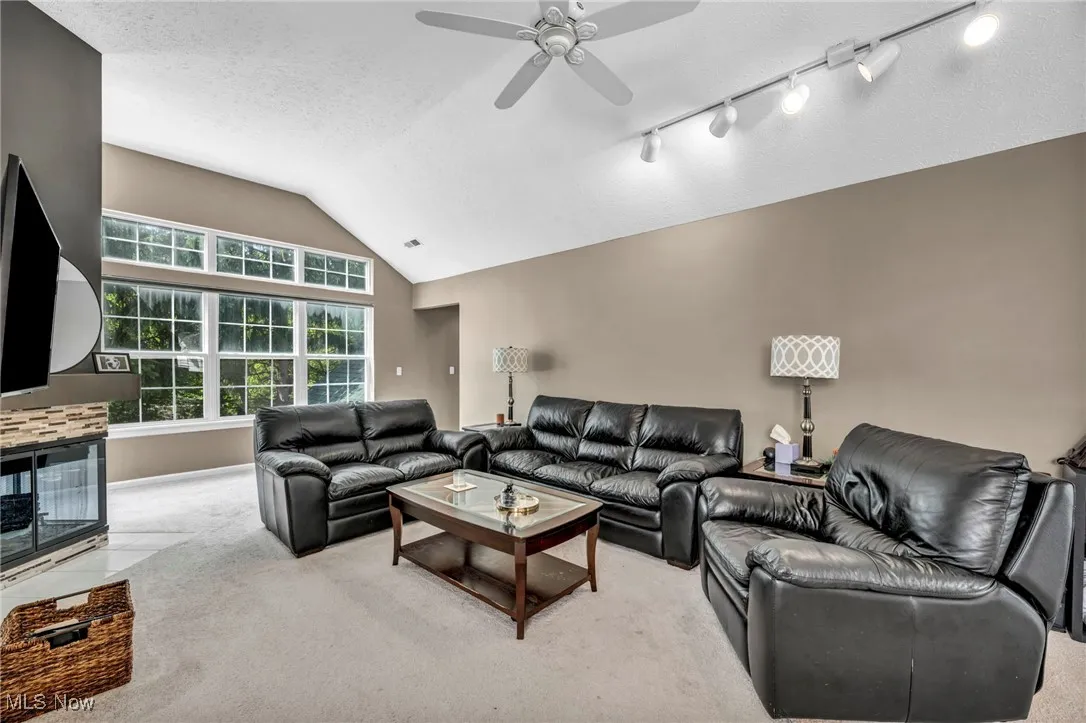 Living room with ceiling fan, carpet floors, vaulted ceiling, and a textured ceiling