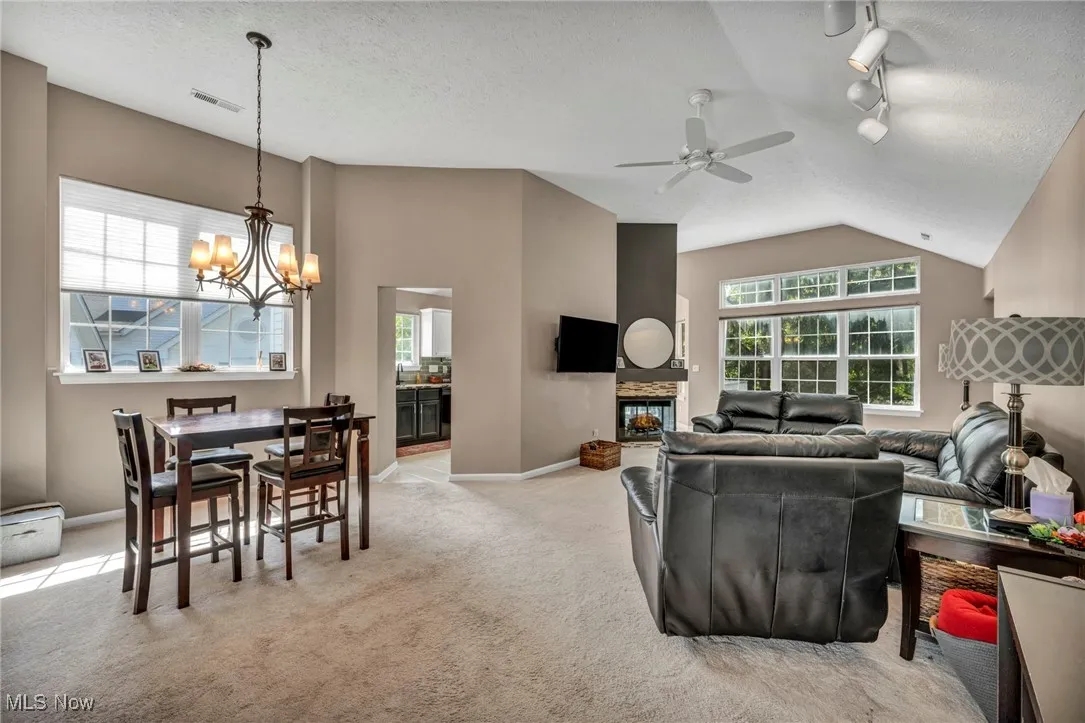 Living room featuring a chandelier, track lighting, a ceiling fan, light colored carpet, and lofted ceiling