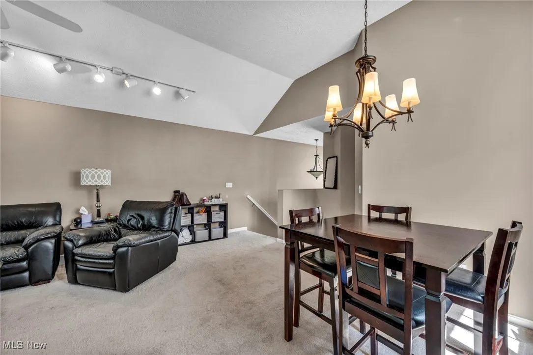 Carpeted dining room featuring a chandelier, vaulted ceiling, and ceiling fan