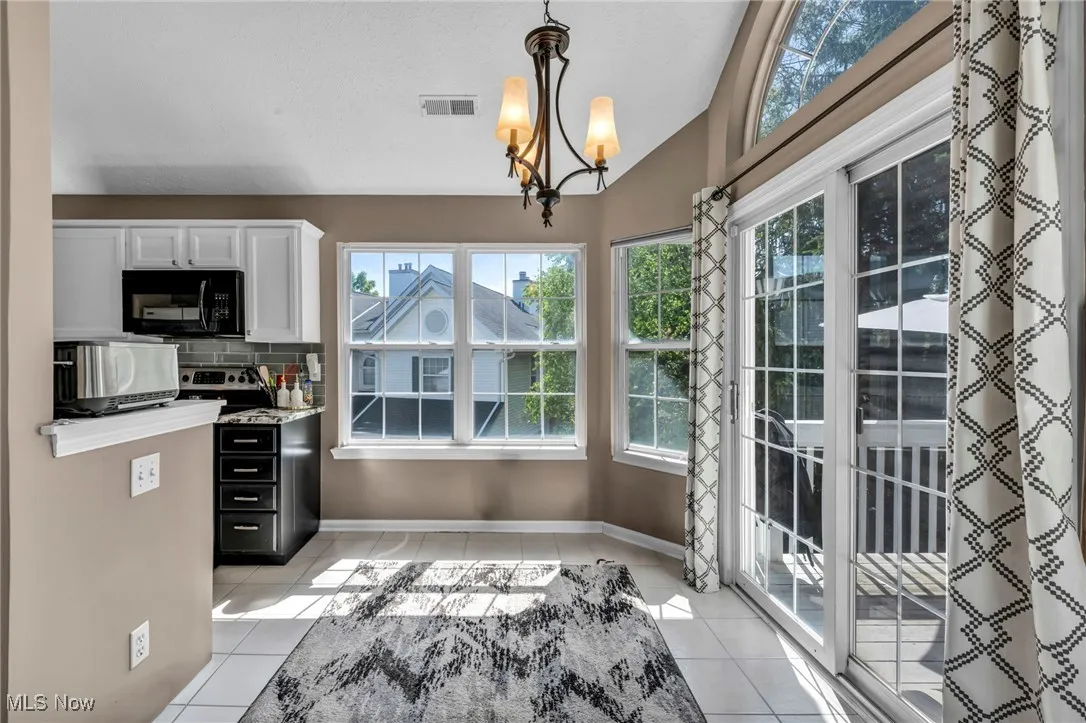 Kitchen featuring black microwave, light tile patterned floors, plenty of natural light, white cabinetry, and vaulted ceiling