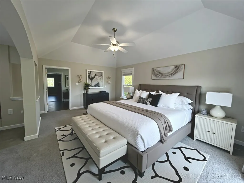 Primary bedroom featuring NEW carpet vaulted ceiling, a ceiling fan, and arched walkways - virtually staged