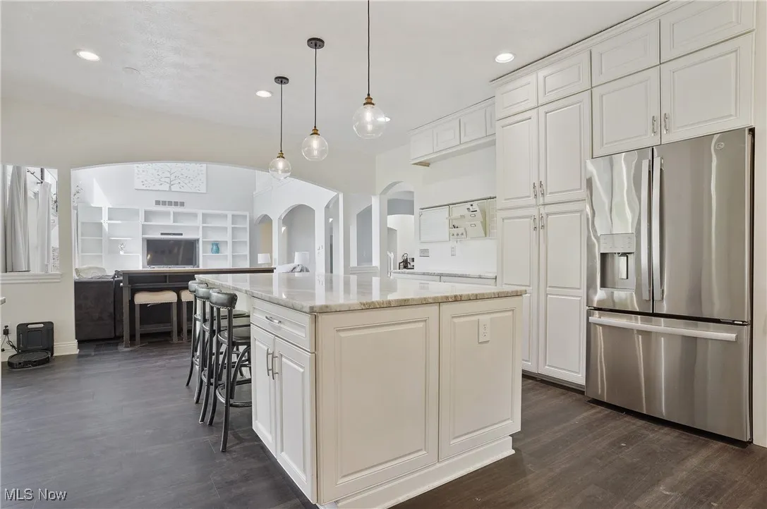 Kitchen featuring stainless steel fridge, arched walkways, new lvt floors, a 9 ft center island, and white cabinetry