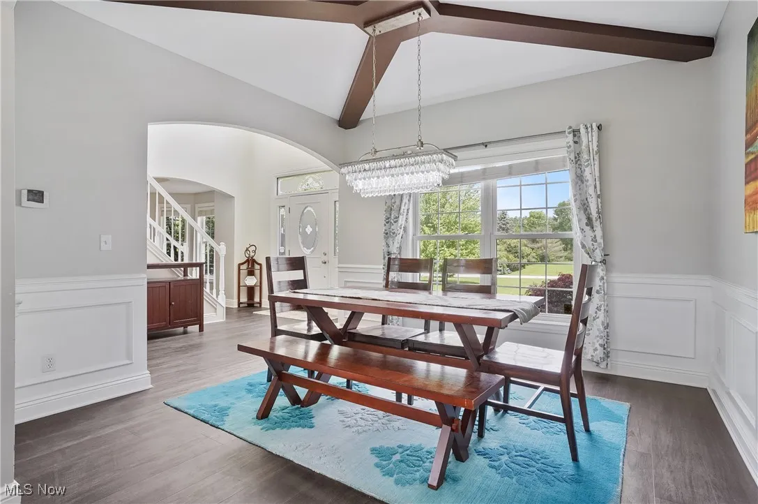 Dining space with arched walkways, wood finished floors, a wainscoted wall, and a chandelier