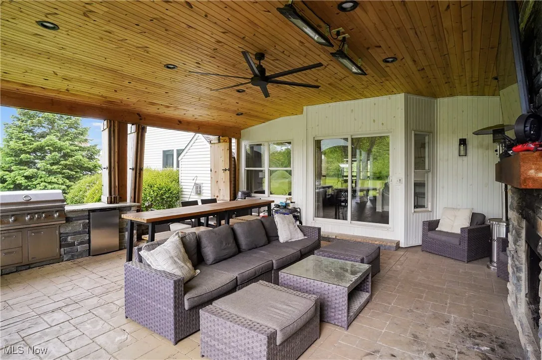 View of patio featuring area for built in grilling area, refrigerator, outdoor lounge area, ceiling fan, stone fireplace with tv