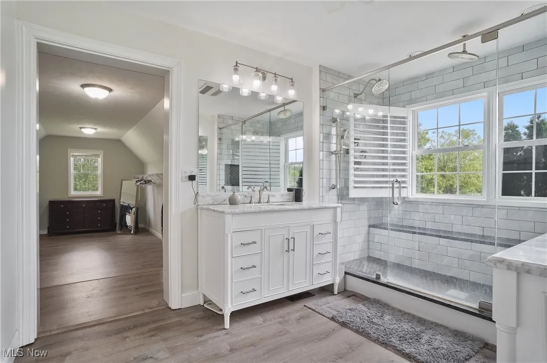 Full bathroom with his/her sink vanities, a large glass/tile shower with bench seating and plantation shutters. open to dream closet/laundry area