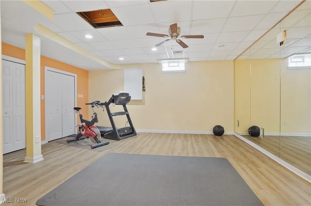 Exercise area in finished basement with lvt floors, ceiling fan, wall of mirrors, shelving and storage closets