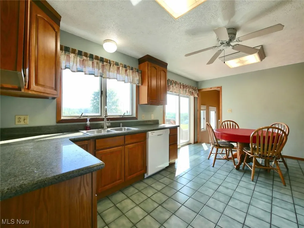 Kitchen featuring white dishwasher, a textured ceiling, dark countertops, light tile patterned floors, and a ceiling fan