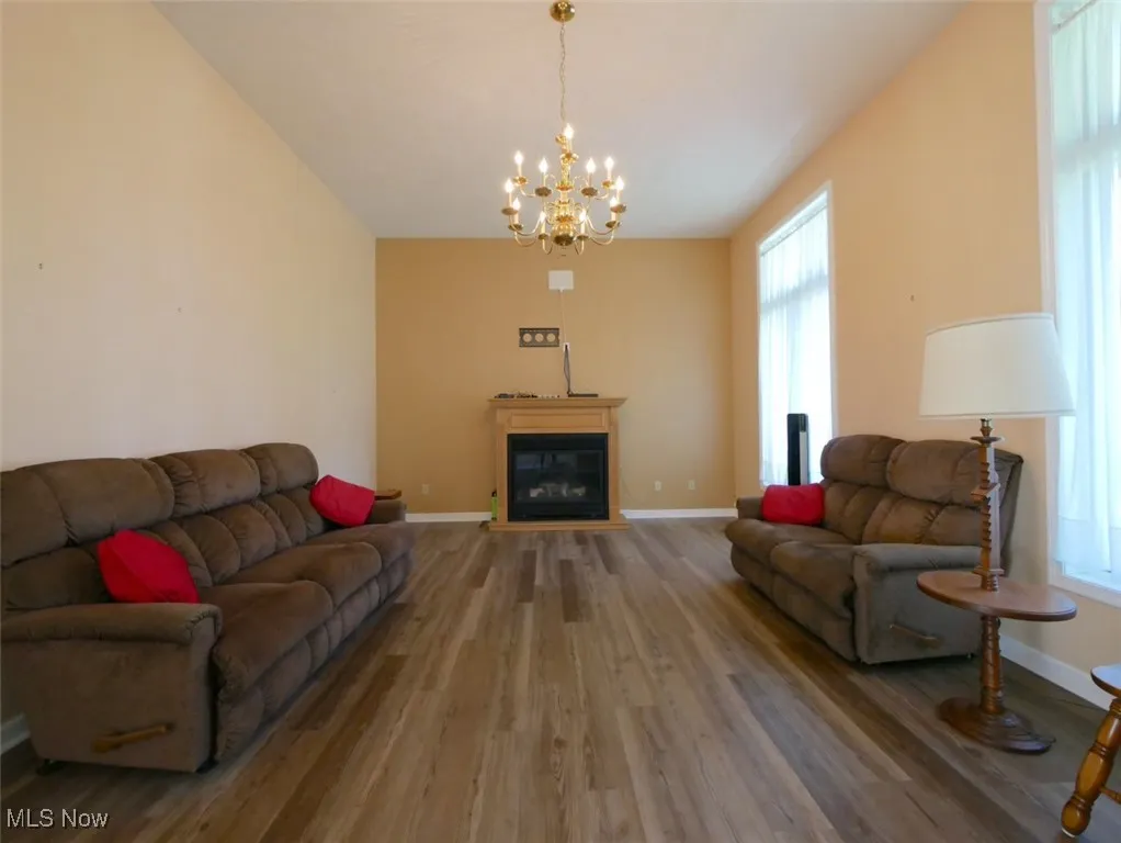 Living room with wood finished floors, a chandelier, a glass covered fireplace, and lofted ceiling
