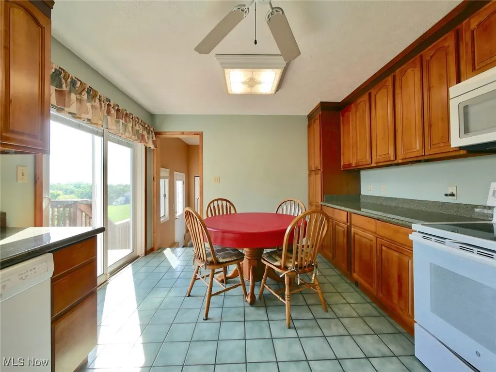 Kitchen featuring white appliances, brown cabinets, light tile patterned floors, and dark countertops