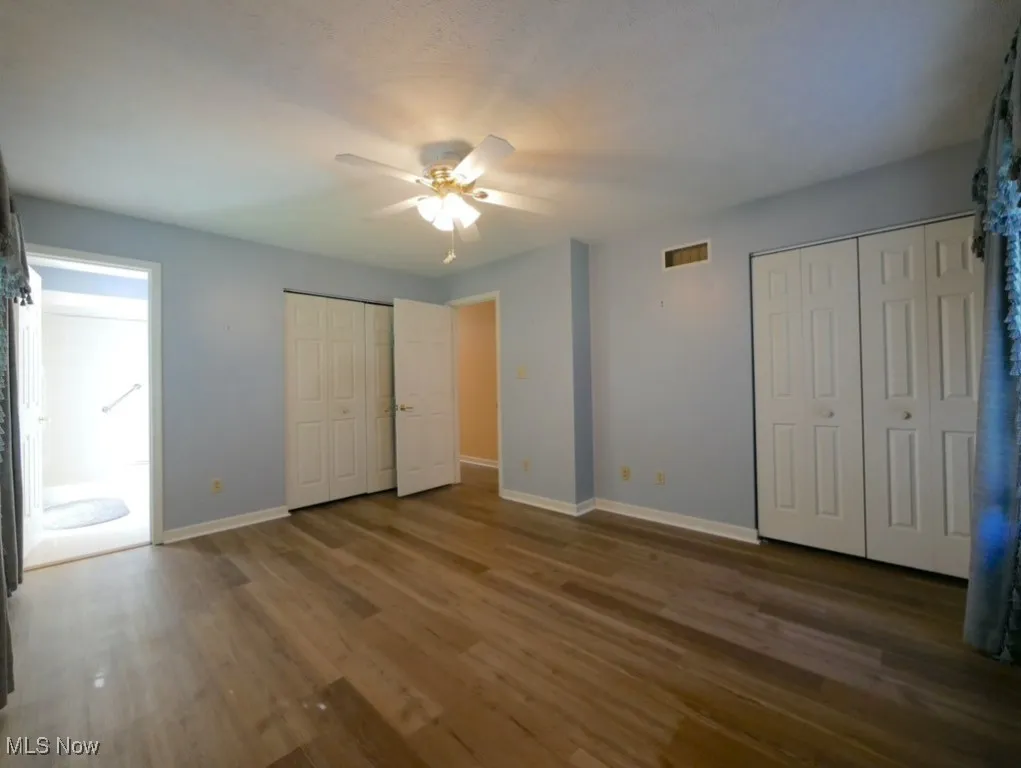 Unfurnished bedroom featuring wood finished floors, two closets, and a ceiling fan