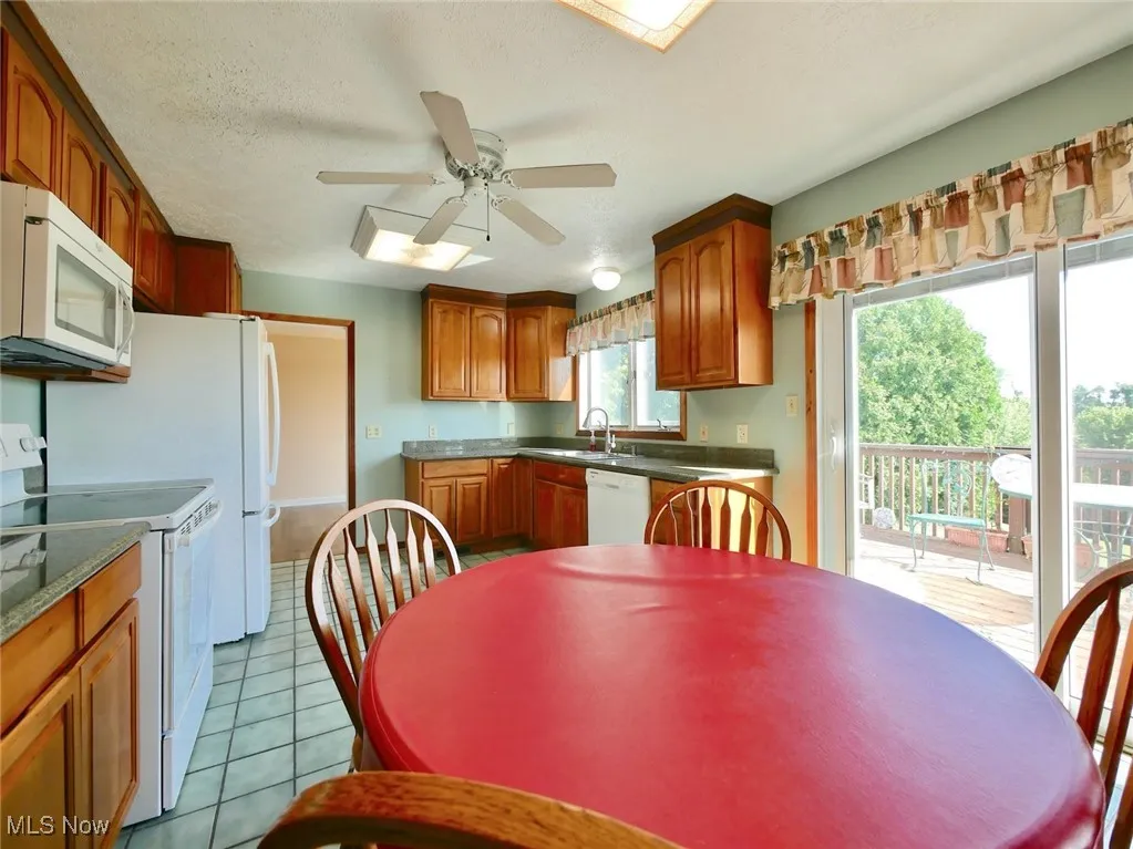 Kitchen with white appliances, a ceiling fan, light tile patterned floors, and brown cabinetry