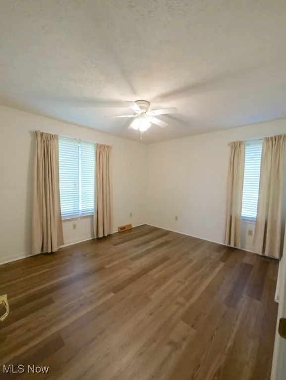 Empty room featuring ceiling fan, wood finished floors, and a textured ceiling