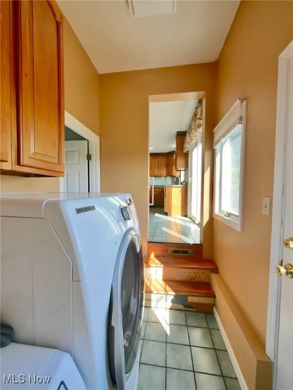 Laundry room with washing machine and dryer, light tile patterned floors, and cabinet space