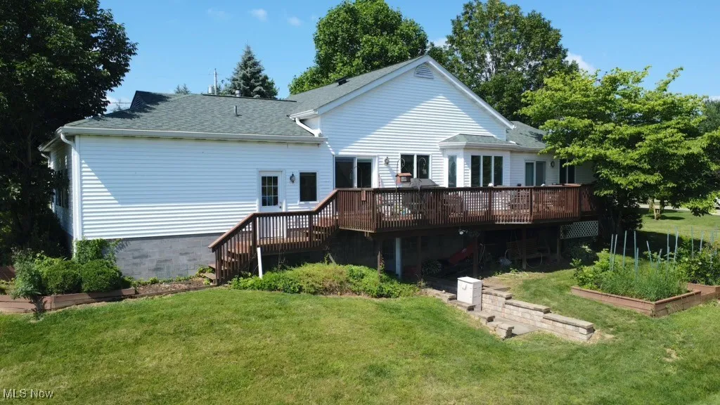 Back of property featuring a vegetable garden, a deck, a yard, a shingled roof, and stairway