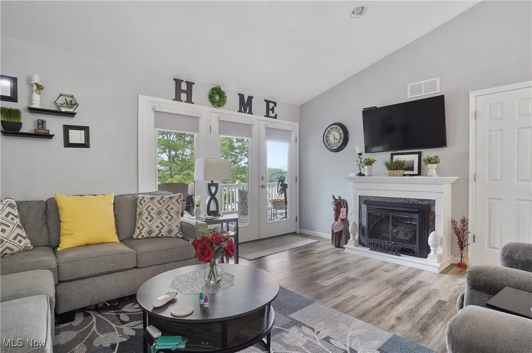 Living area featuring lofted ceiling, wood finished floors, a premium fireplace, and french doors