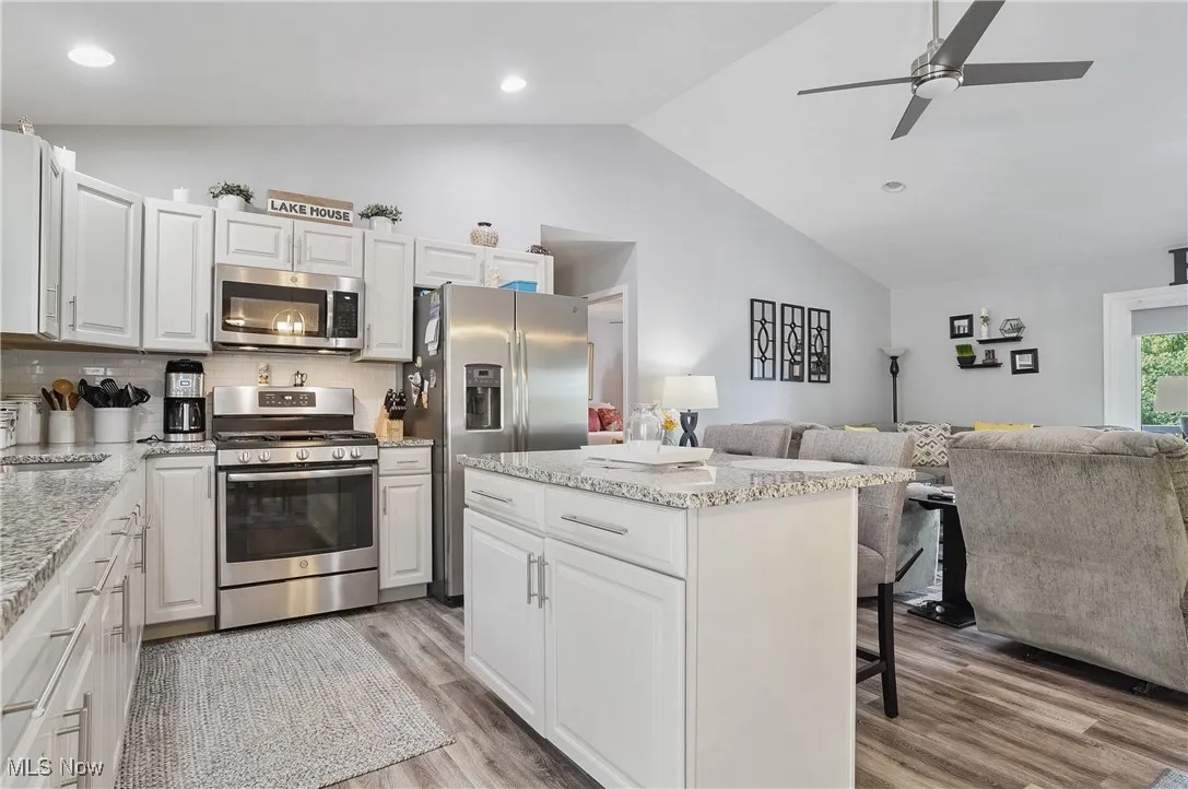 Kitchen with appliances with stainless steel finishes, open floor plan, vaulted ceiling, a breakfast bar, and light wood-type flooring