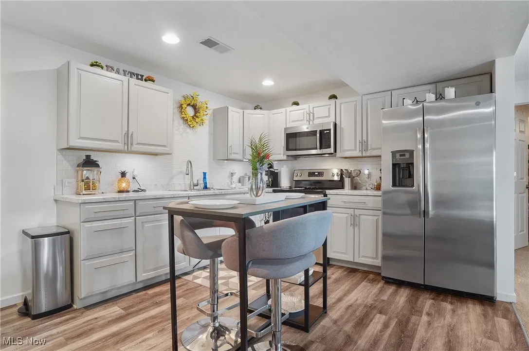 Kitchen with stainless steel appliances, light wood-style floors, decorative backsplash, light countertops, and recessed lighting