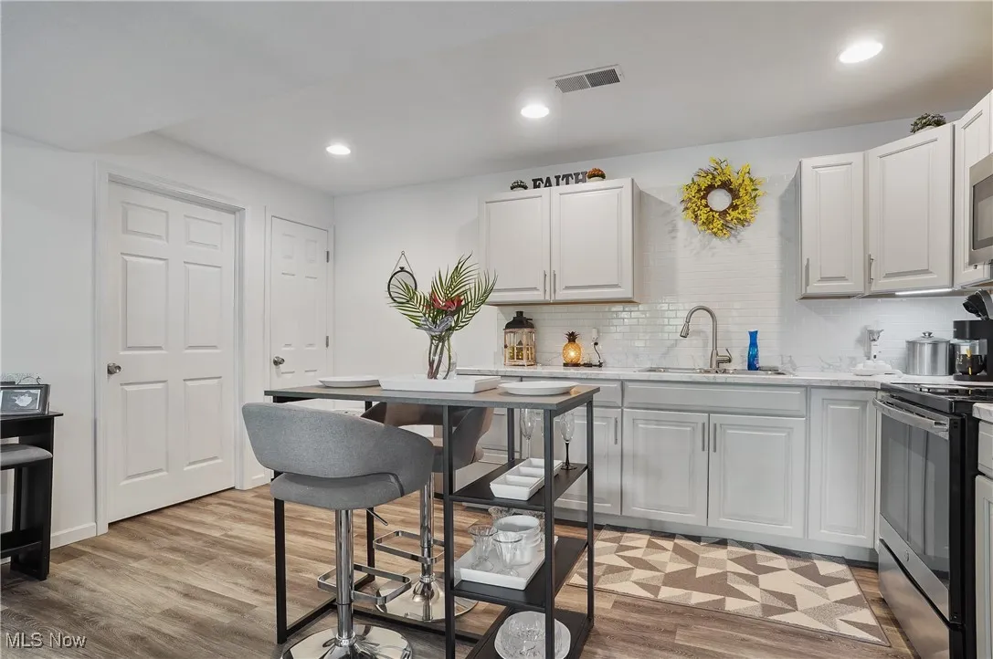 Kitchen with appliances with stainless steel finishes, backsplash, light wood-style floors, white cabinets, and recessed lighting