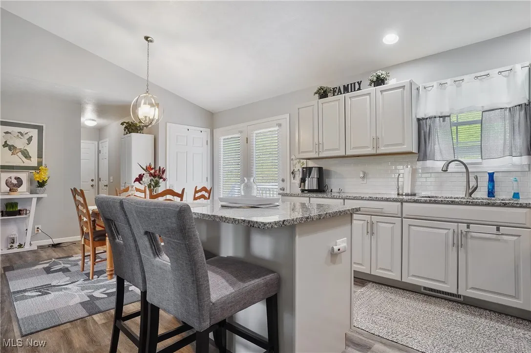 Kitchen with lofted ceiling, a breakfast bar area, tasteful backsplash, light stone countertops, and a kitchen island