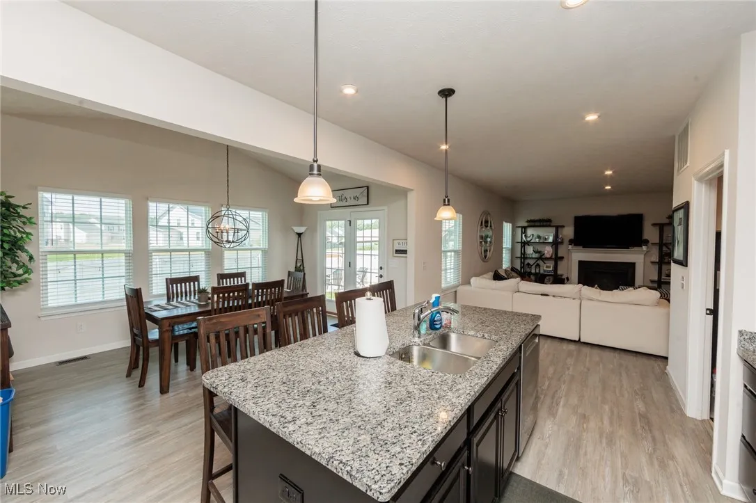 Kitchen with stainless steel dishwasher, light wood-style flooring, a fireplace, a center island with sink, and decorative light fixtures