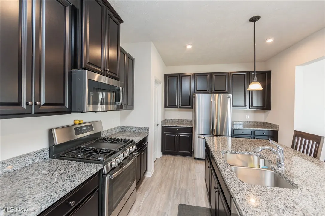 Kitchen featuring stainless steel appliances, light wood-style flooring, decorative light fixtures, light stone counters, and recessed lighting