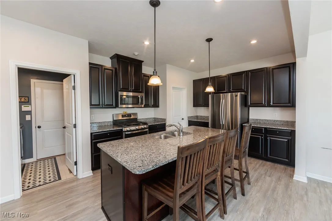 Kitchen with stainless steel appliances, a kitchen bar, light wood-style floors, light stone countertops, and a center island with sink