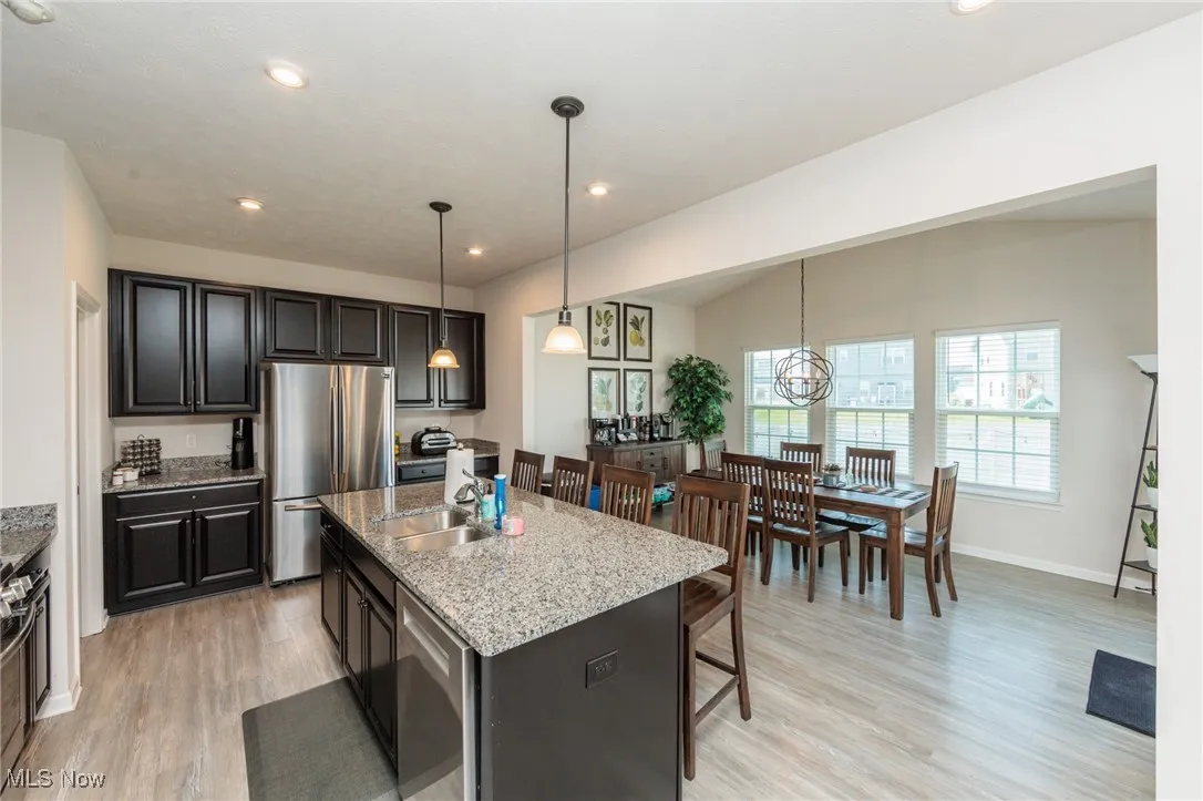 Kitchen with appliances with stainless steel finishes, light wood finished floors, a kitchen breakfast bar, light stone countertops, and an island with sink