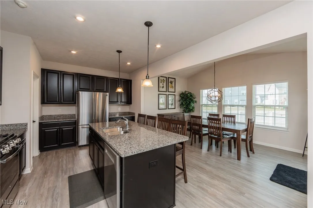 Kitchen featuring a kitchen breakfast bar, appliances with stainless steel finishes, light wood finished floors, light stone counters, and vaulted ceiling