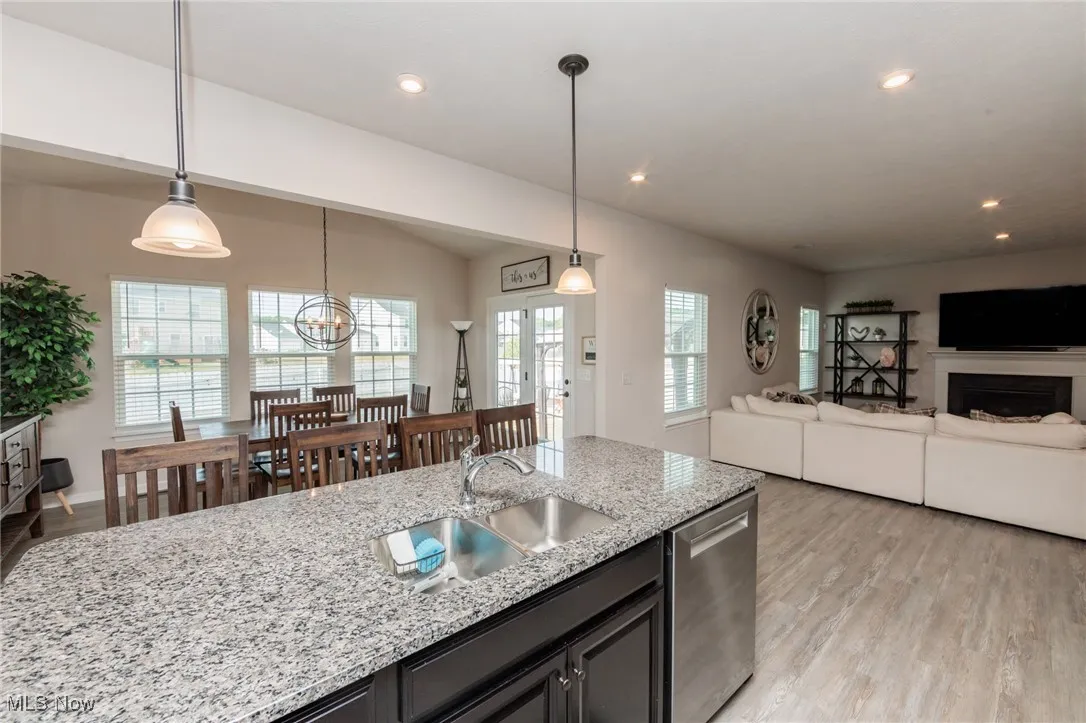 Kitchen with light wood finished floors, dishwasher, recessed lighting, light stone countertops, and hanging light fixtures