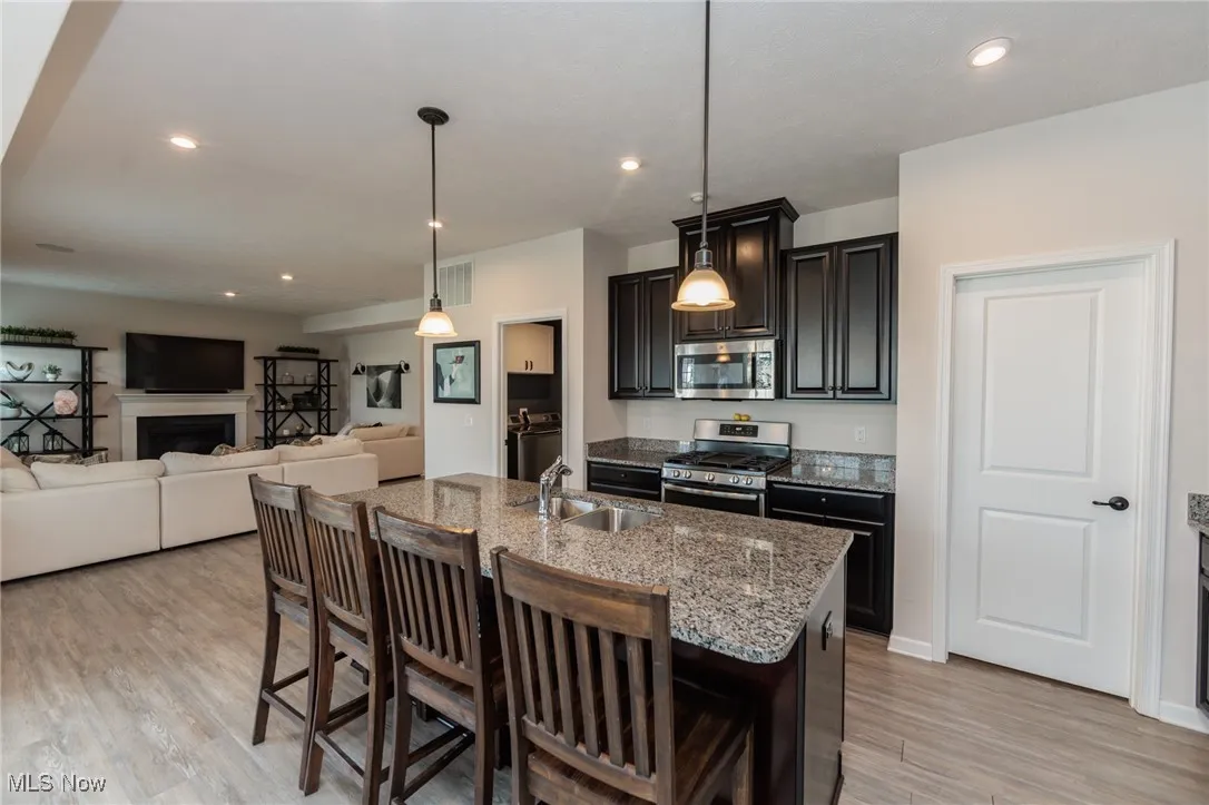 Kitchen featuring a kitchen bar, stainless steel appliances, a kitchen island with sink, light stone countertops, and recessed lighting