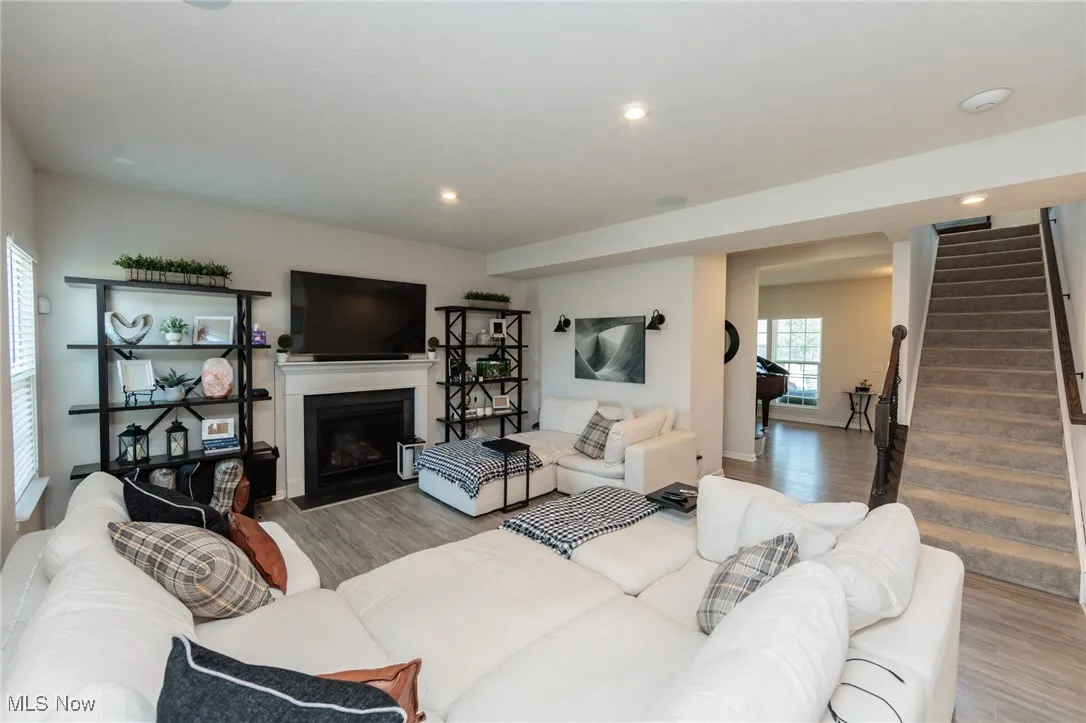 Living area with wood finished floors, stairs, a fireplace with flush hearth, and recessed lighting