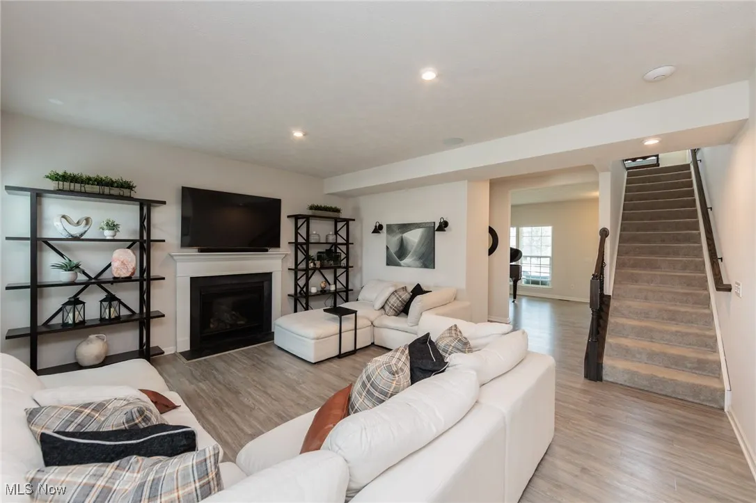 Living area featuring stairway, light wood-style flooring, a fireplace with flush hearth, and recessed lighting