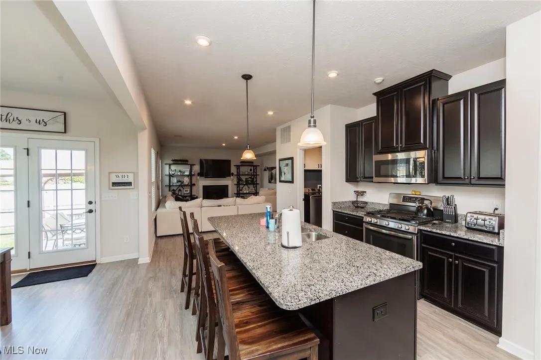 Kitchen with stainless steel appliances, light wood-style flooring, light stone countertops, a breakfast bar, and open floor plan
