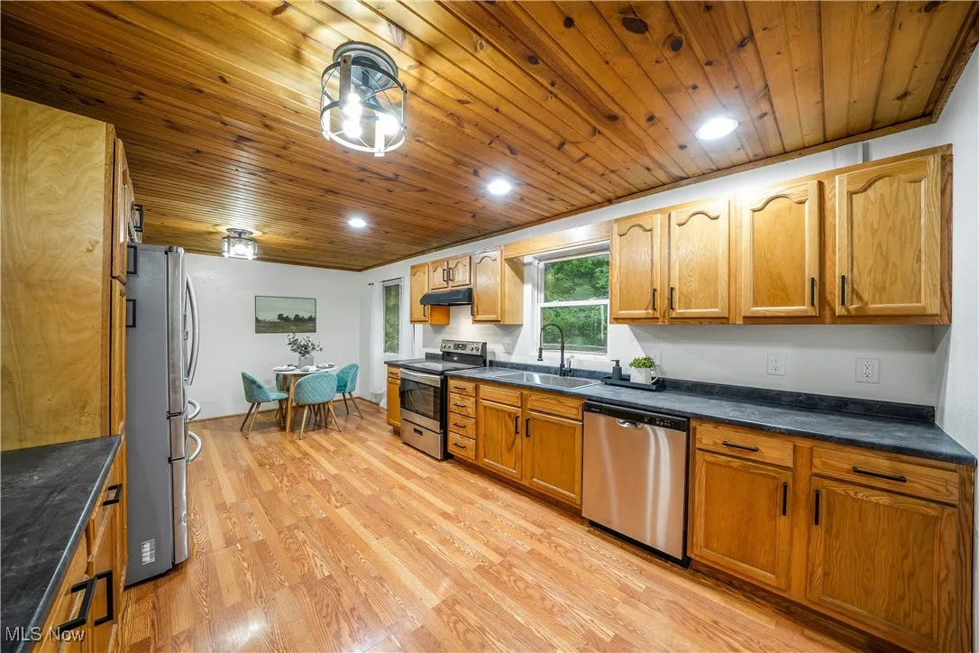 Kitchen with stainless steel appliances, wood ceiling, light wood finished floors, under cabinet range hood, and brown cabinetry