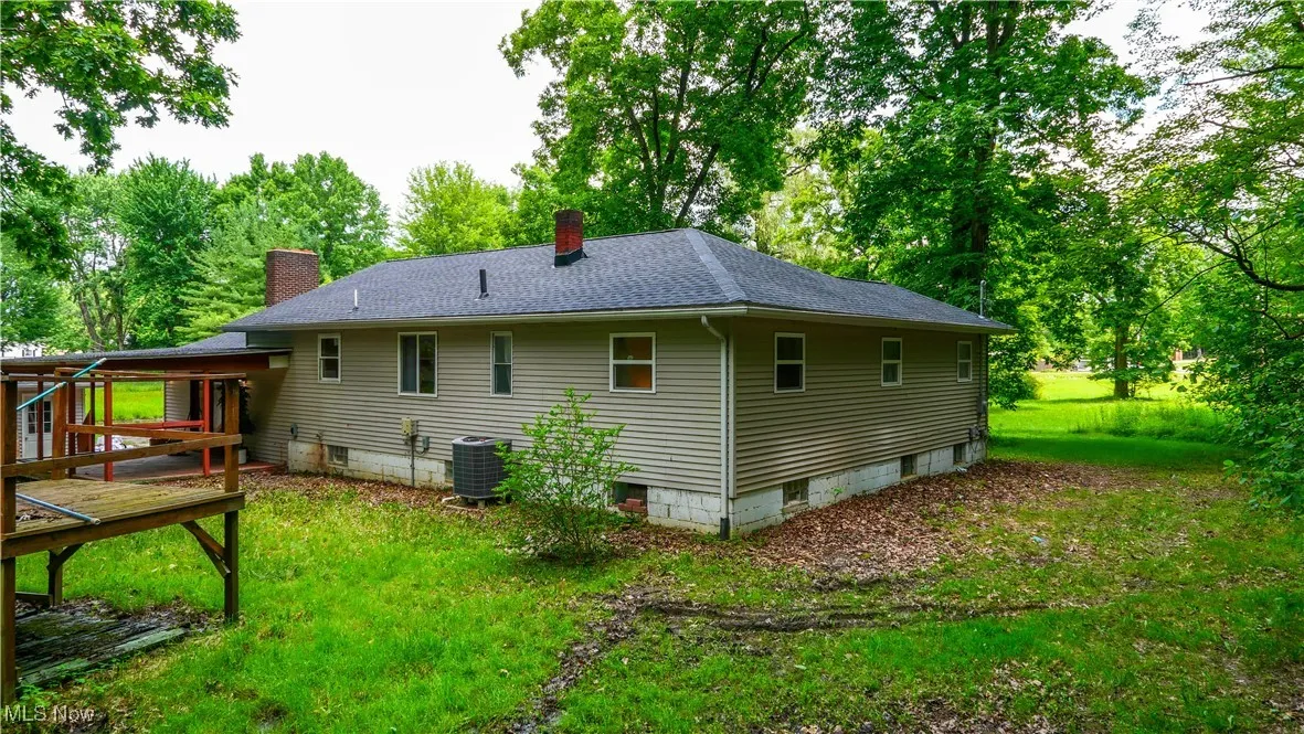 Back of property featuring a chimney, a deck, roof with shingles, a yard, and view of scattered trees