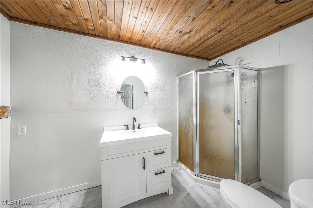 Bathroom featuring marble finish flooring, a textured wall, wood ceiling, vanity, and a shower stall