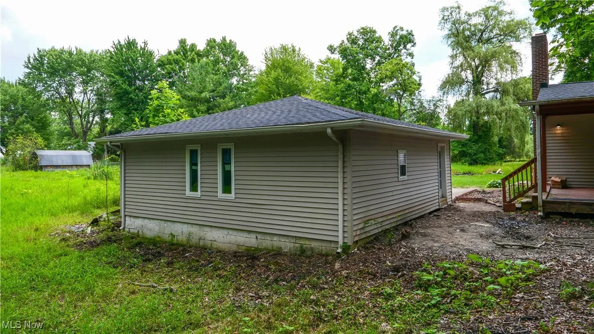 View of side of home with roof with shingles and view of wooded area