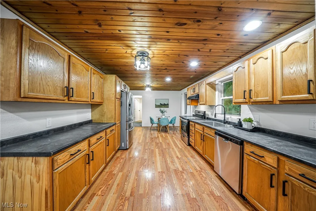 Kitchen with stainless steel appliances, wood ceiling, light wood-type flooring, under cabinet range hood, and brown cabinetry